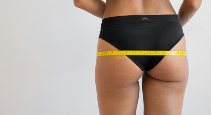 Close-up of hips with measuring tape, highlighting body assessment in a minimalist setting.