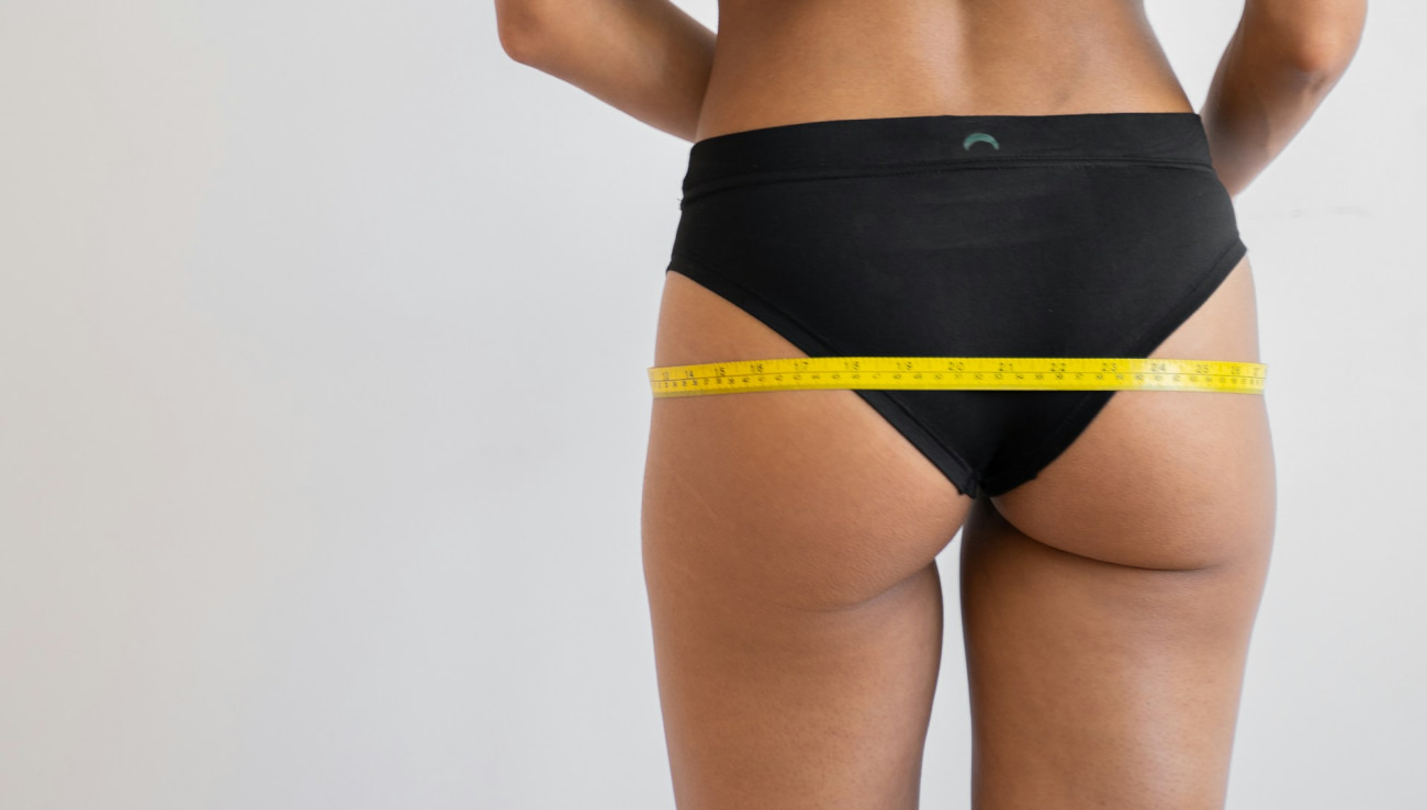 Close-up of hips with measuring tape, highlighting body assessment in a minimalist setting.