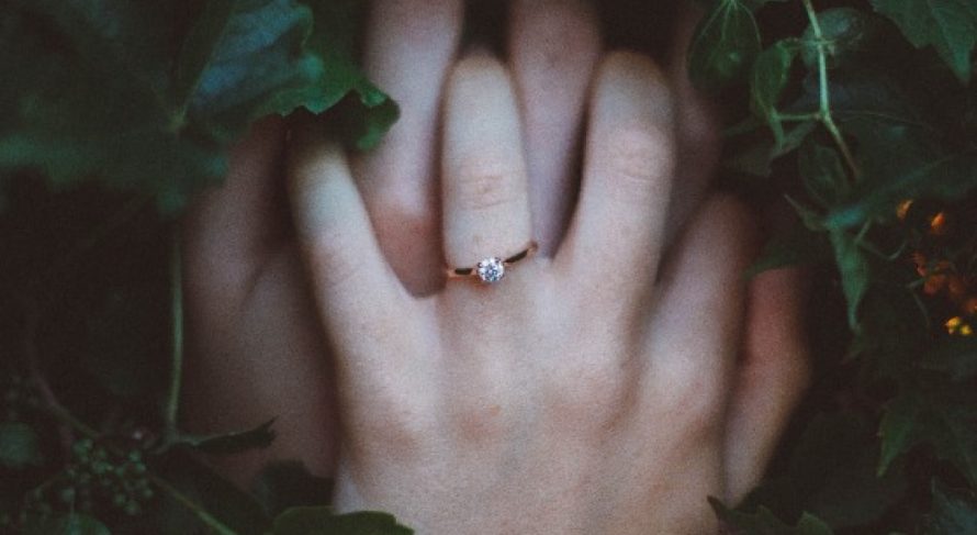 Intertwined hands showcase an elegant engagement ring amidst lush greenery, symbolizing love and commitment.