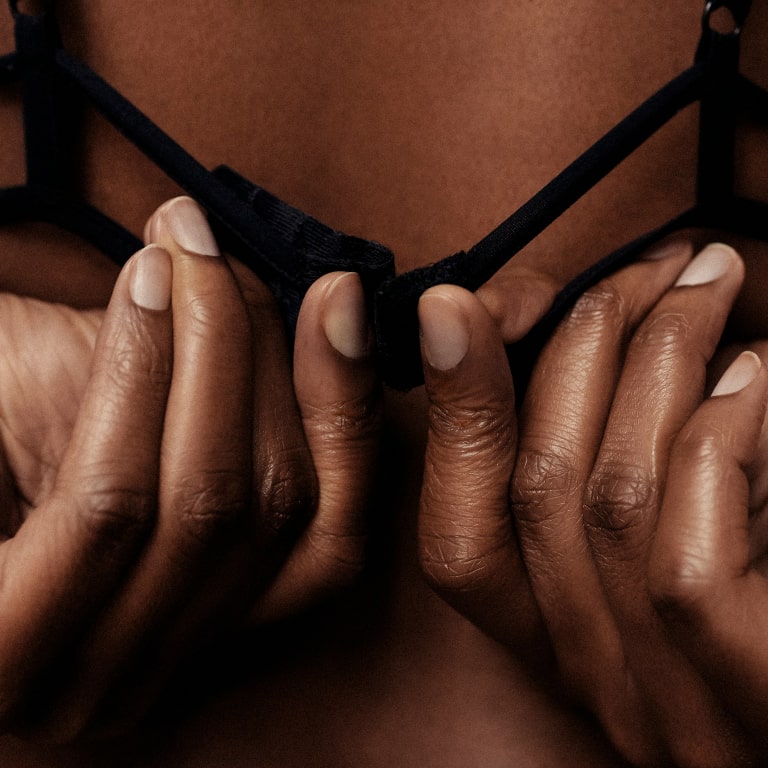 Elegant hands grasping a black bra, symbolizing intimacy and self-care in soft lighting.