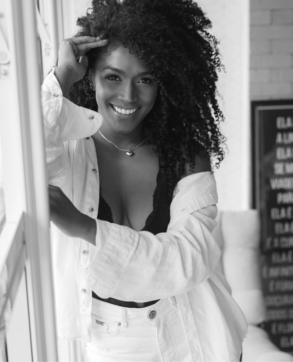 Elegant black and white portrait of a joyful woman with curly hair in a stylish outfit.