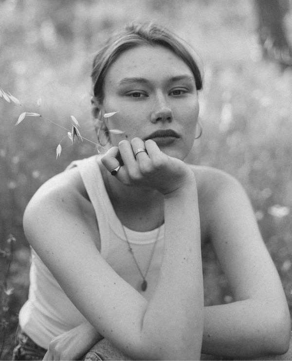 Black-and-white portrait of a young woman thoughtfully seated in a serene meadow.