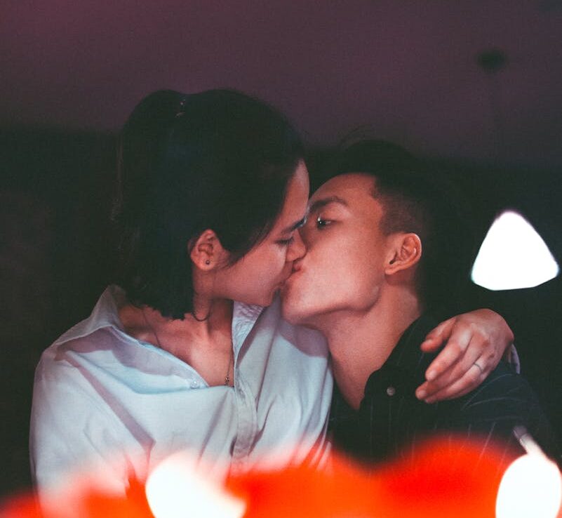 A romantic kiss shared by an Asian couple, captured in a warm, intimate setting.