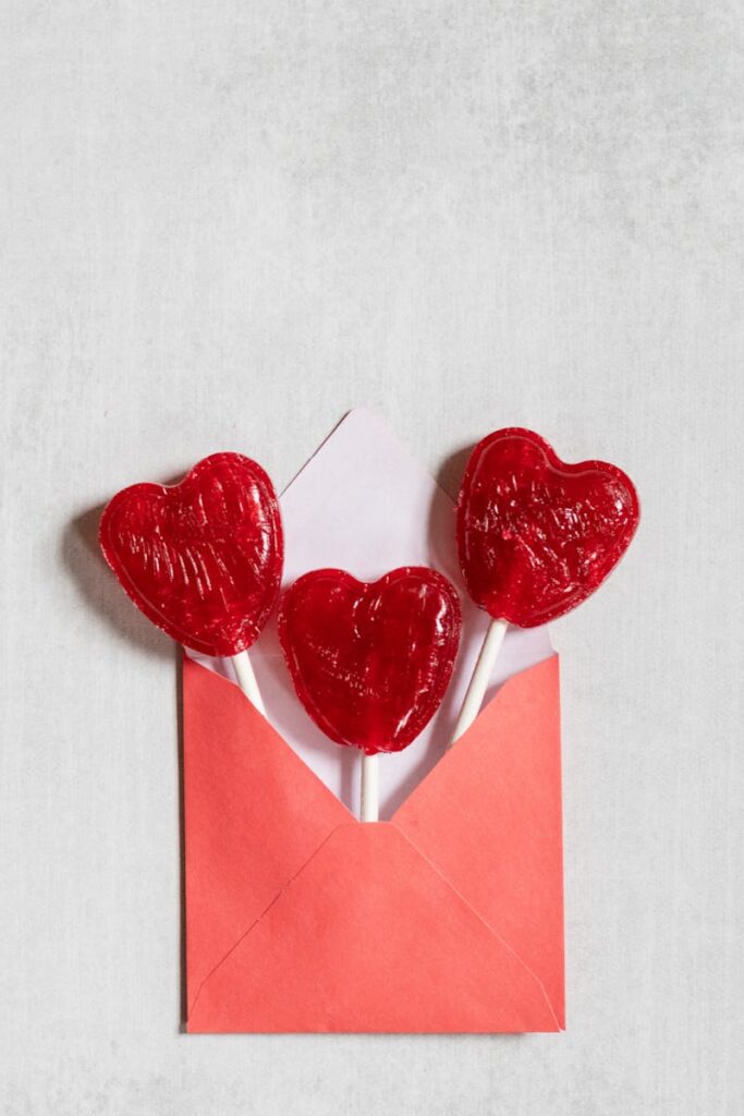 Trois sucettes rouges en forme de cœur sortent d'une enveloppe rouge, parfaite pour les célébrations de la Saint-Valentin.