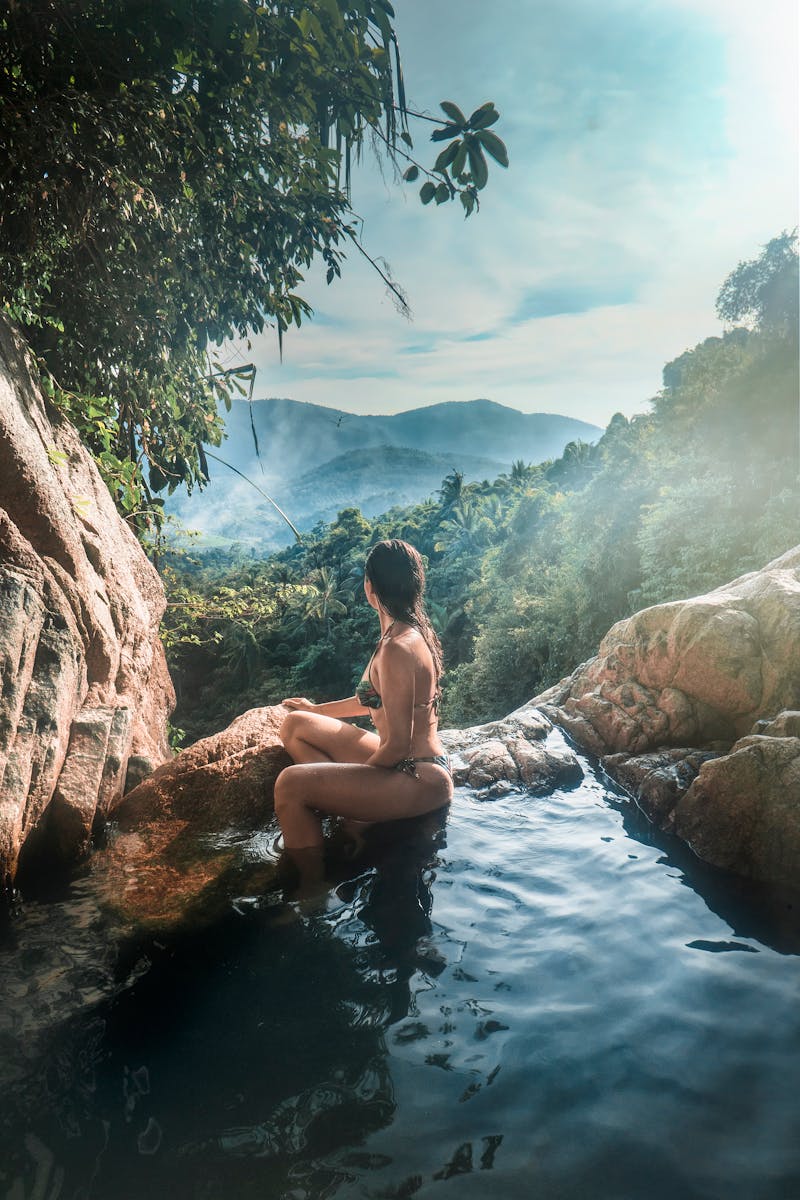 En kvinna i baddräkt kopplar av vid ett vattenfall med grönskande berg i Ko Samui, Thailand.