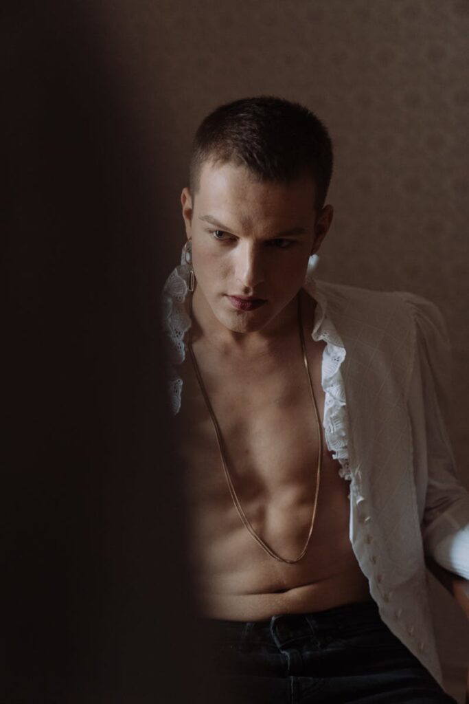 Fashionable indoor portrait of a shirtless man in a white shirt with frills, creating a dramatic mood.