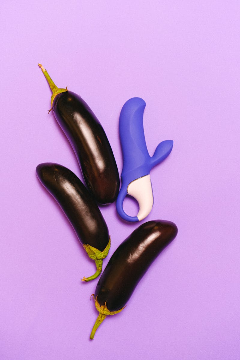 Levendige afbeelding van aubergines en een blauwe vibrator op paarse achtergrond.