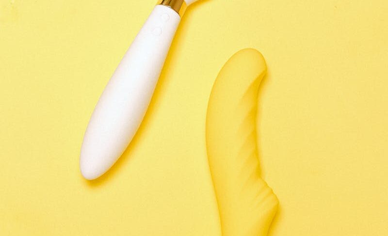 Bright flat lay of silicone sex toys on vibrant yellow backdrop.