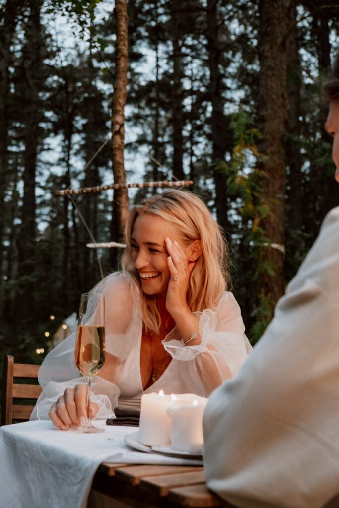 Une femme profite d'un dîner romantique en plein air avec du champagne et des bougies dans un cadre forestier serein.