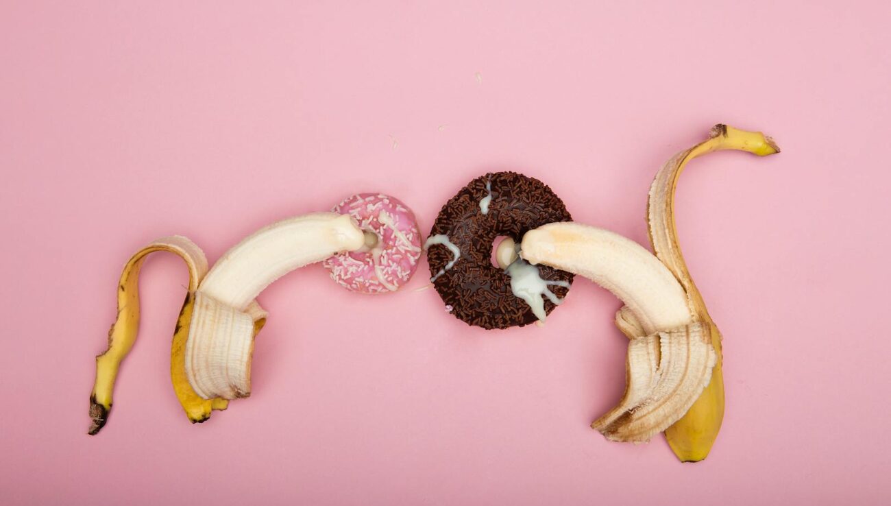 Legende arrangement af skrællede bananer og donuts på en lyserød baggrund, perfekt til konceptuel kunst.