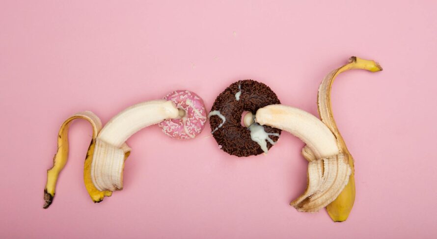 Playful arrangement of peeled bananas and donuts on a pink background, perfect for conceptual art.