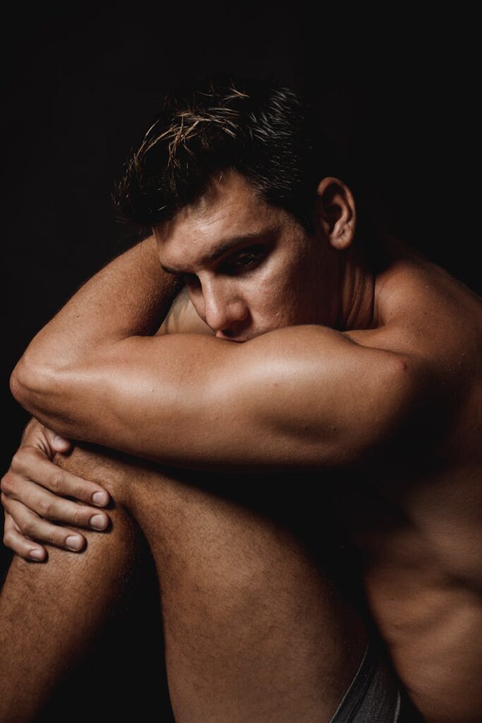 Dramatic portrait of a shirtless man sitting, deep in thought, in a studio setting.