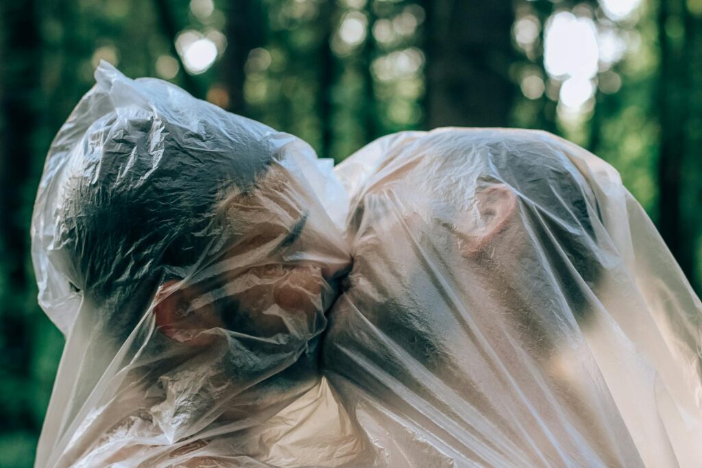 Una pareja se abraza y se besa bajo una cubierta de plástico en un entorno forestal.