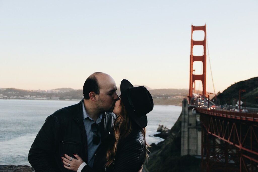 man och kvinna kysser varandra vid Golden Gate Bridge under dagtid