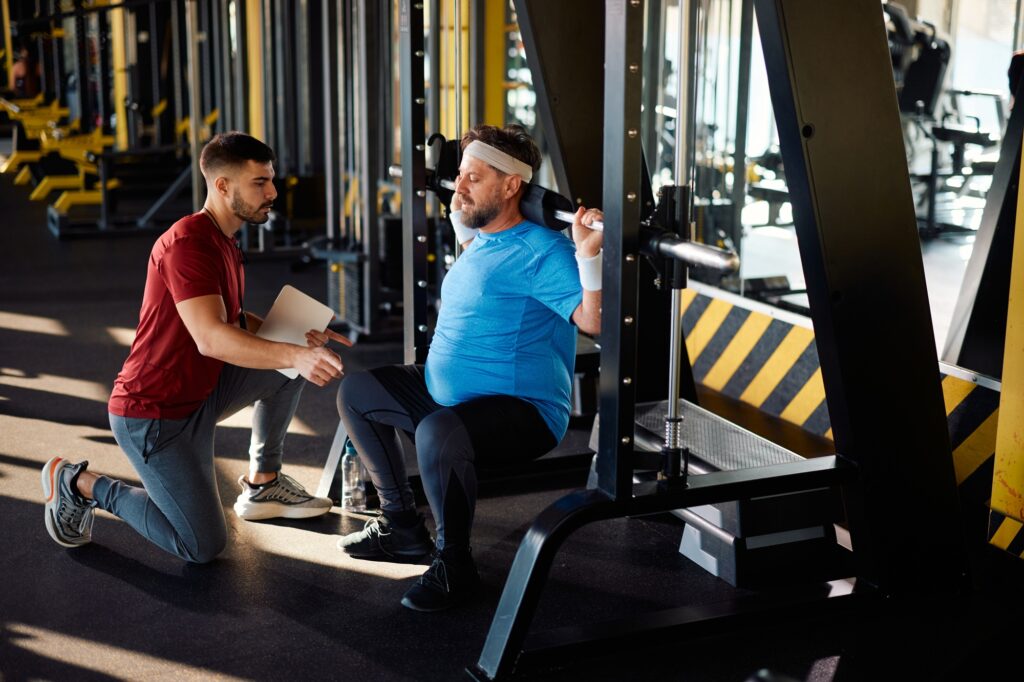 Mogen man tränar på en träningsmaskin under en träningsklass med personlig tränare på ett gym.