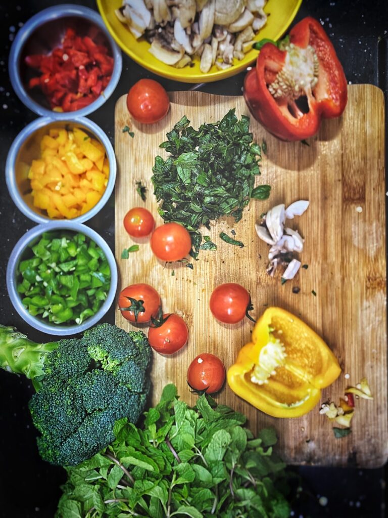 tomates cor de laranja perto de pimentos amarelos fatiados, brócolos numa tábua de cortar madeira