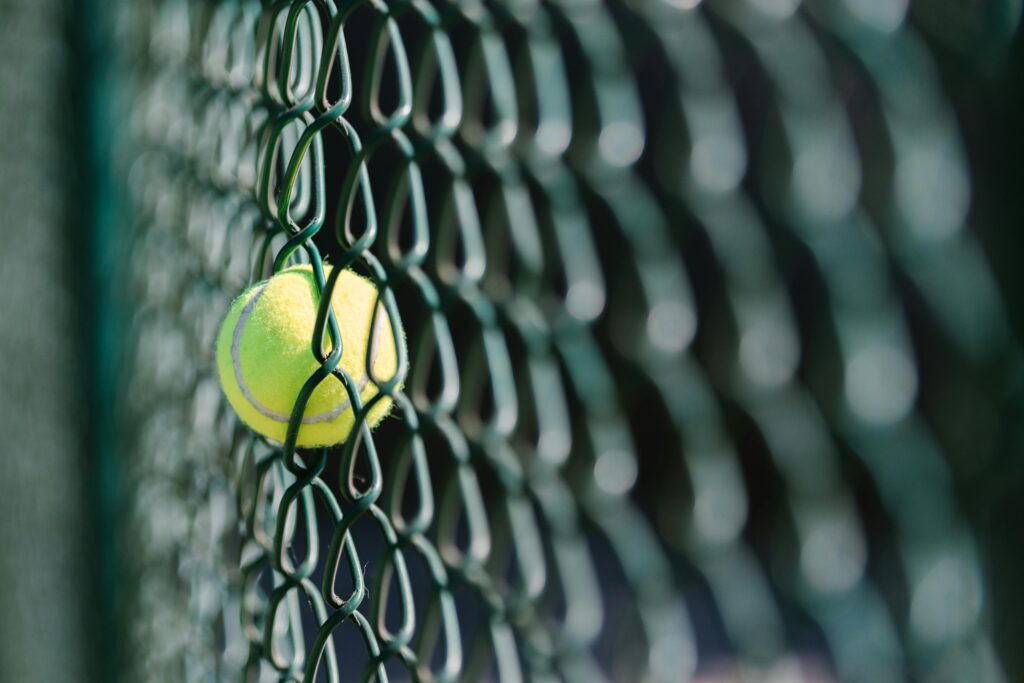 Pelota de tenis atrapada en una alambrada verde, símbolo de momentos inesperados en el deporte.