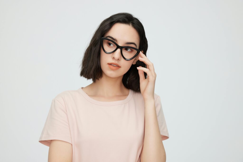 Jeune femme élégante portant des lunettes œil de chat, incarnant la confiance et l'accessibilité sur un fond minimaliste.