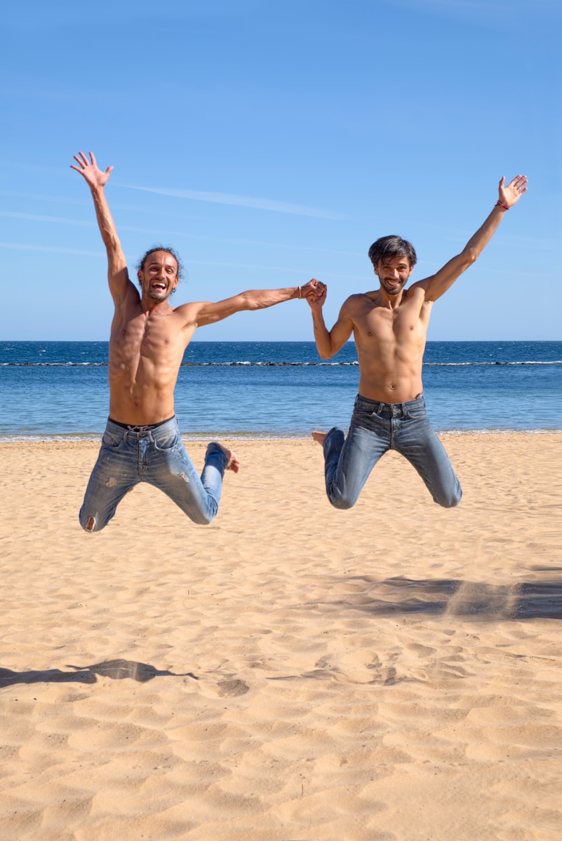 deux hommes sautant au-dessus du sable d'une plage brune